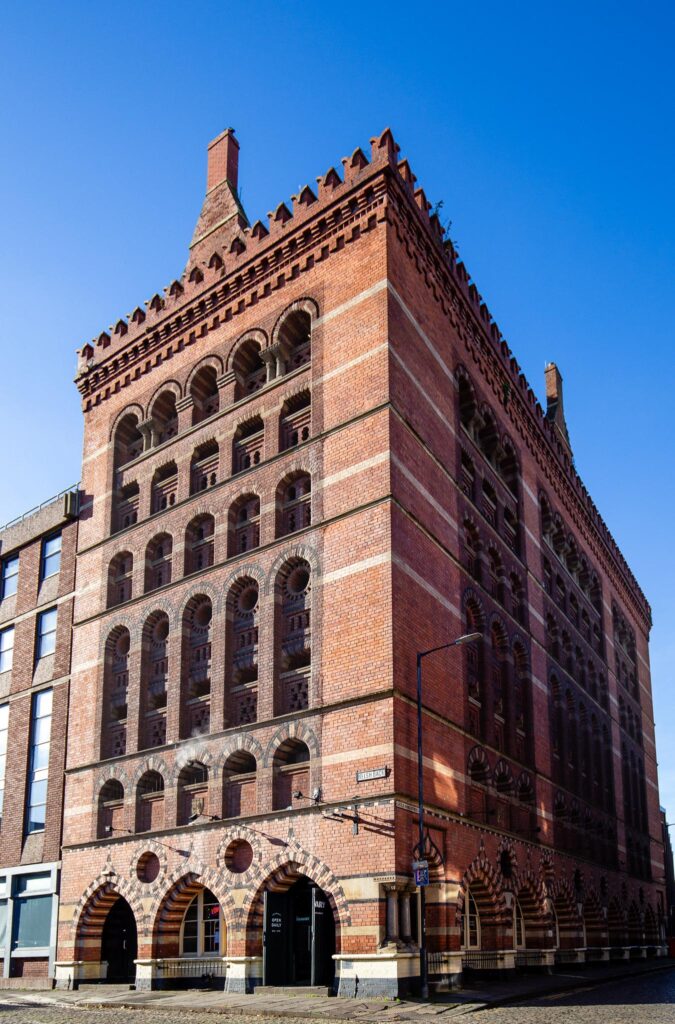 The tall red and black brick facade of The Granary, with rows of arched windows, against a blue sky