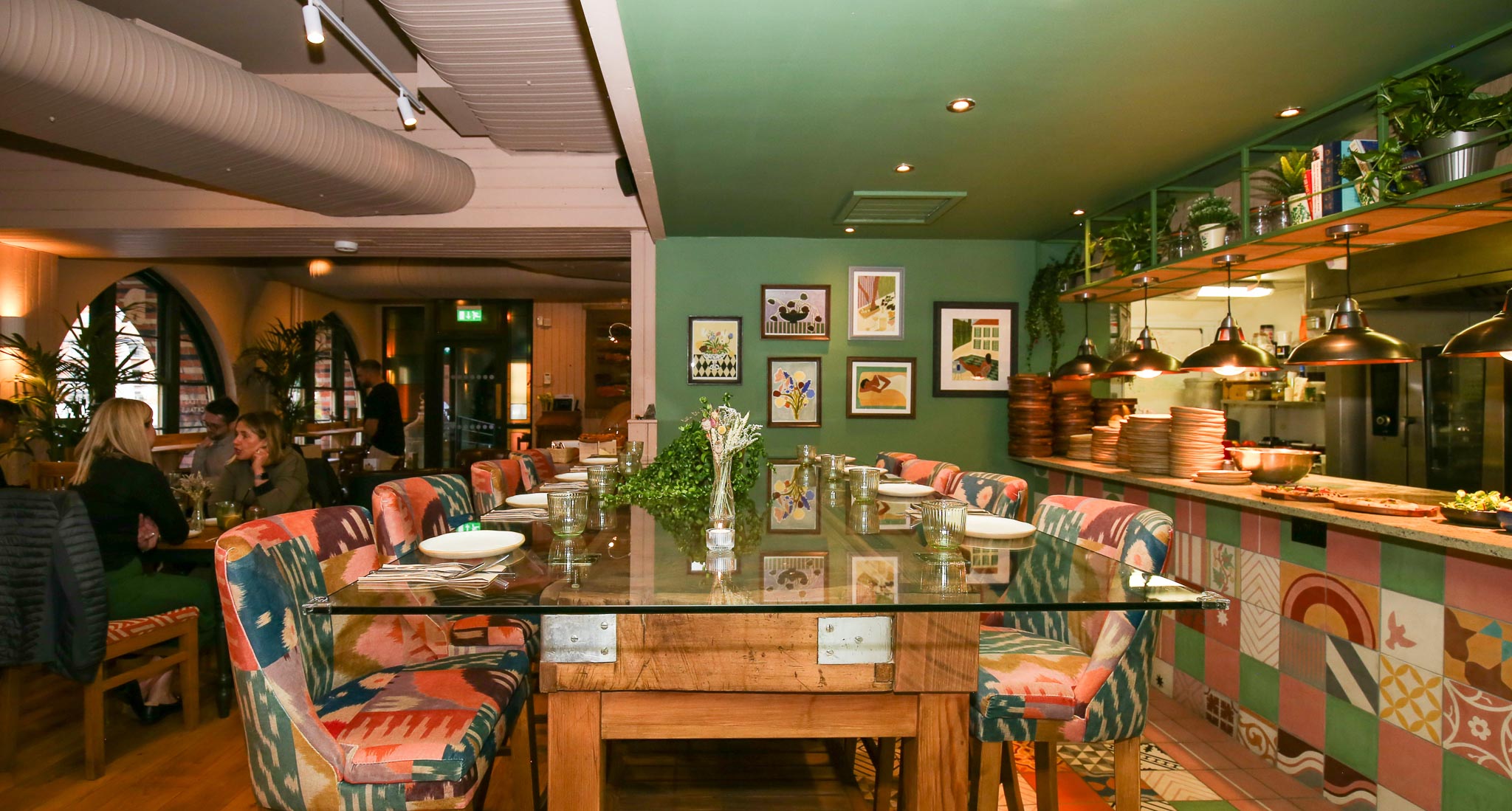 The Chef's Table, a century-old butcher's block restored with a glass top, with patterned upholstered chairs beside the tiled open kitchen at The Granary