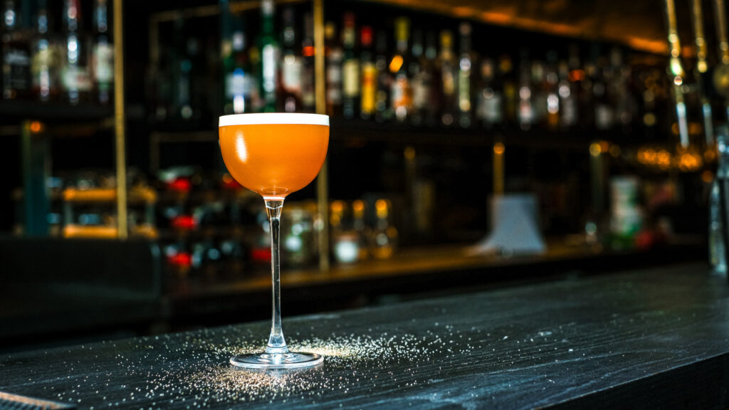 An orange cocktail in a coupe glass on the bar at The Granary Club