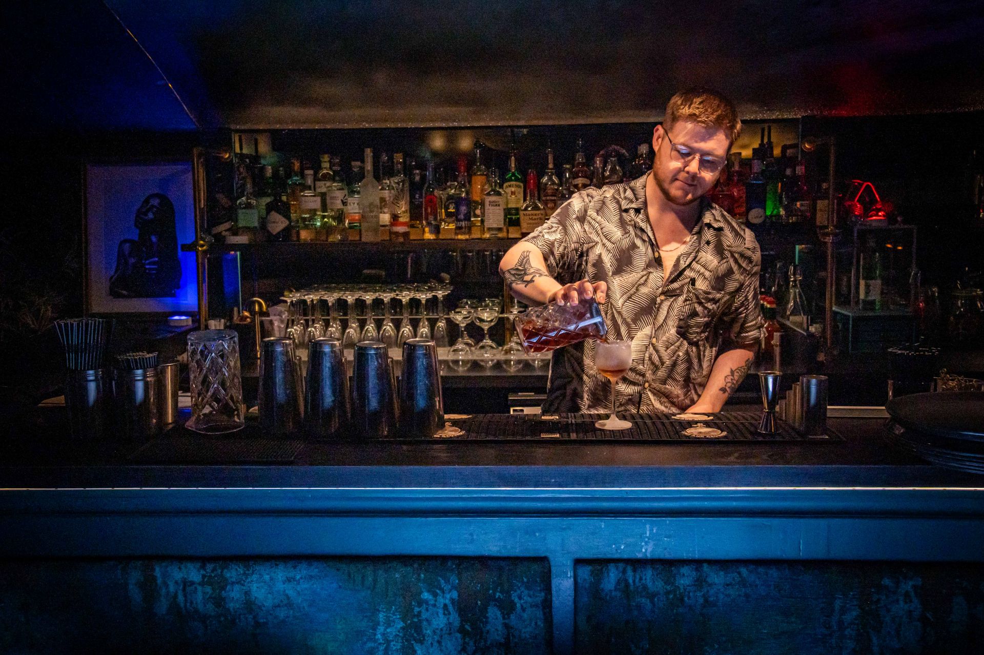 A bartender pouring a cocktail behind the blue-lit bar in The Granary Club