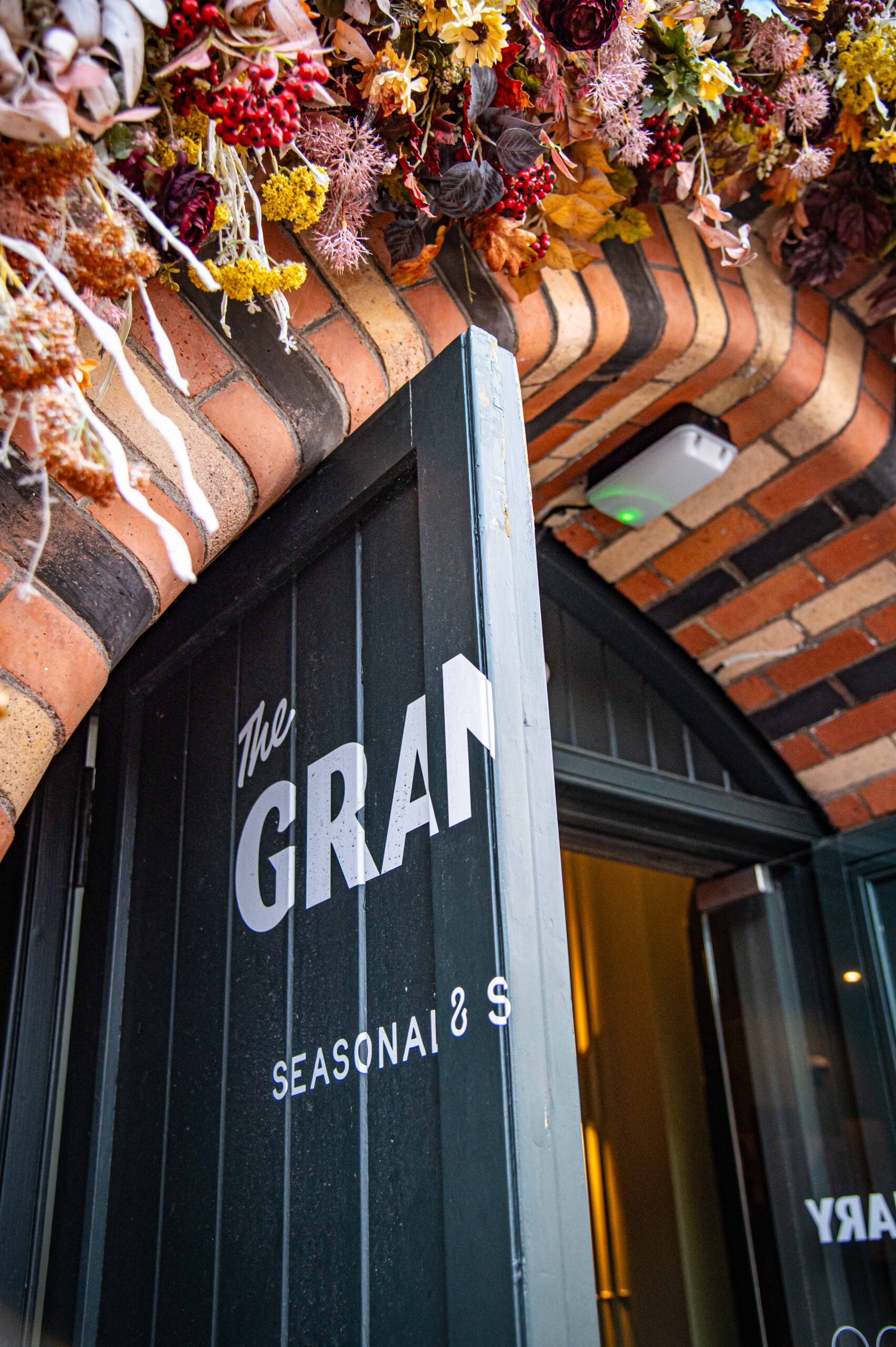 The open front door of The Granary, painted dark green with the restaurant's name, beneath a brick arch decorated with dried flowers