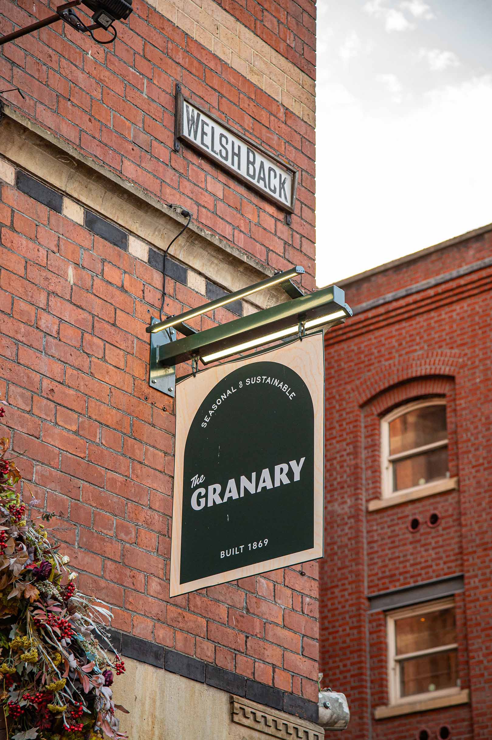 The Welsh Back street sign above The Granary's dark green hanging sign, reading "The Granary, Built 1869", on the red brick corner of the building