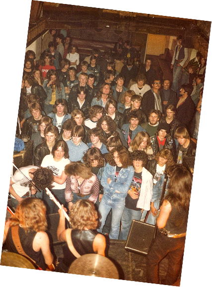 A packed crowd in front of the stage at a rock night, in a faded colour photo
