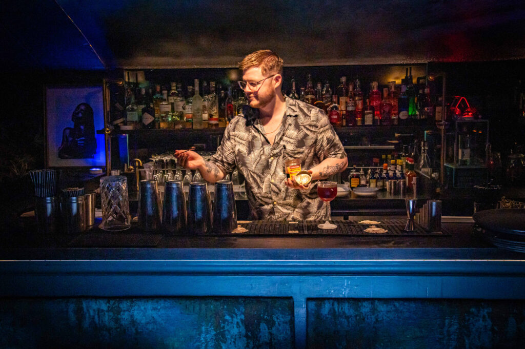 A bartender serving cocktails at the blue-lit bar in The Granary Club