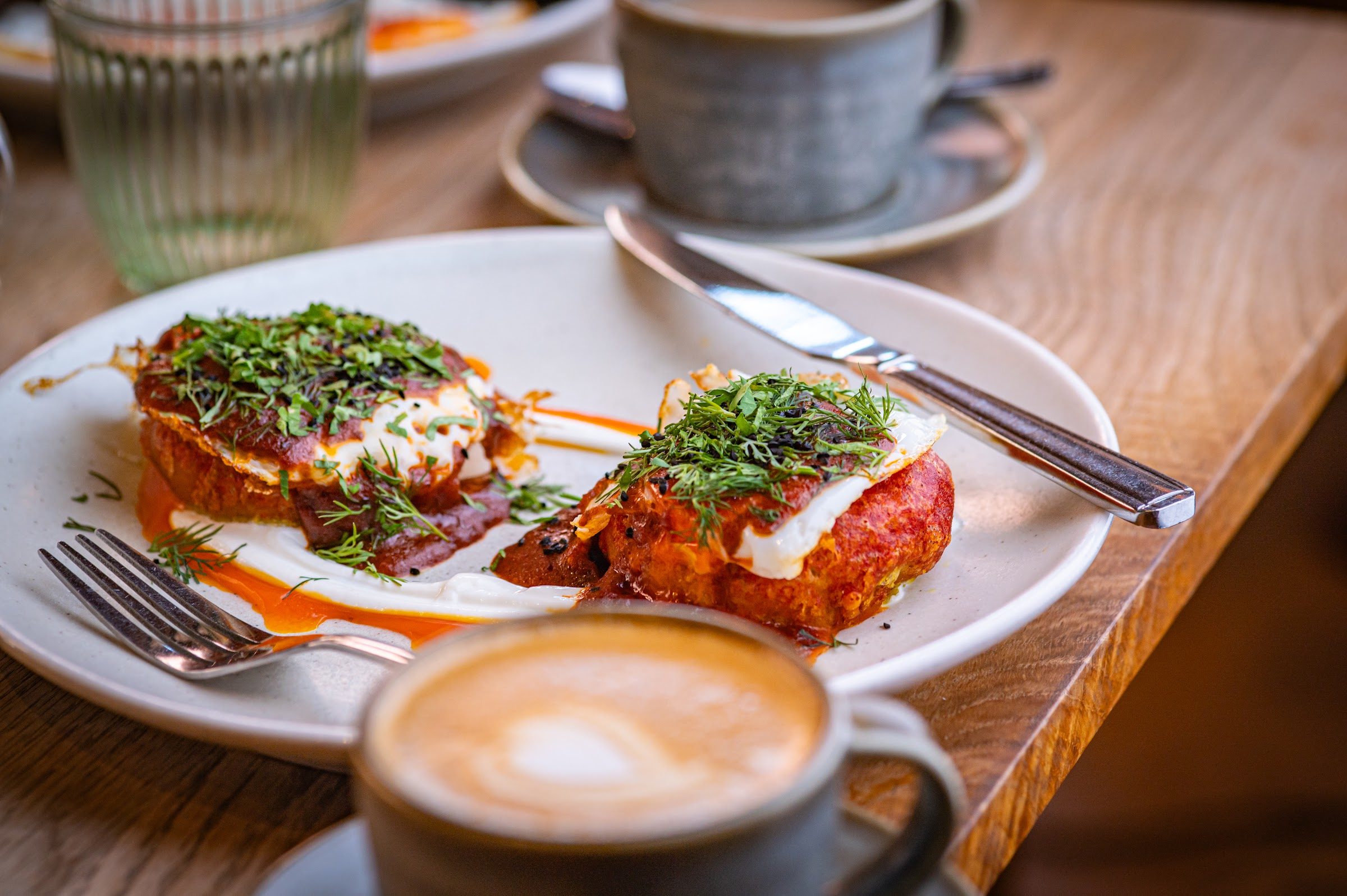 A flat white with latte art beside Maakouda potato cakes with harissa and tomato sauce, fried egg and soft herbs at The Granary