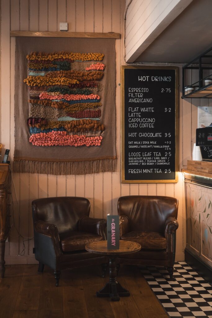 A colourful woven wall hanging above two leather armchairs beside the hot drinks board at The Granary